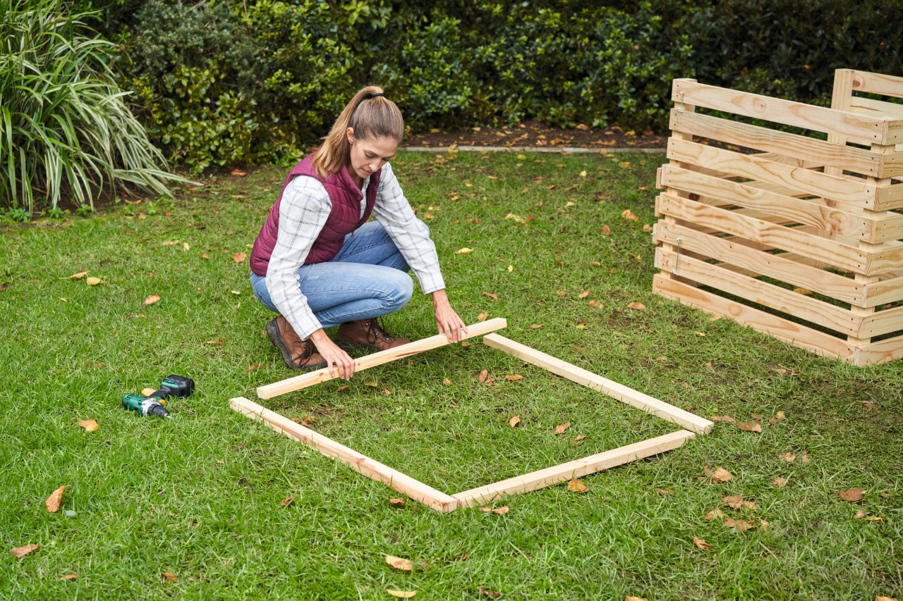 Uma mulher dispõe num gramado ripas perpendiculares entre si para formar a moldura da composteira de madeira para jardim.