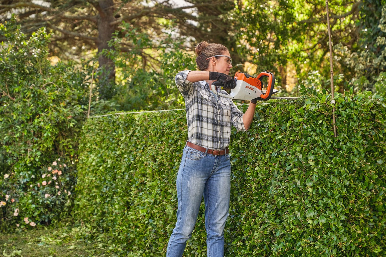 Uma mulher a topiar um arbusto com uma podadora a bateria STIHL HSA 45