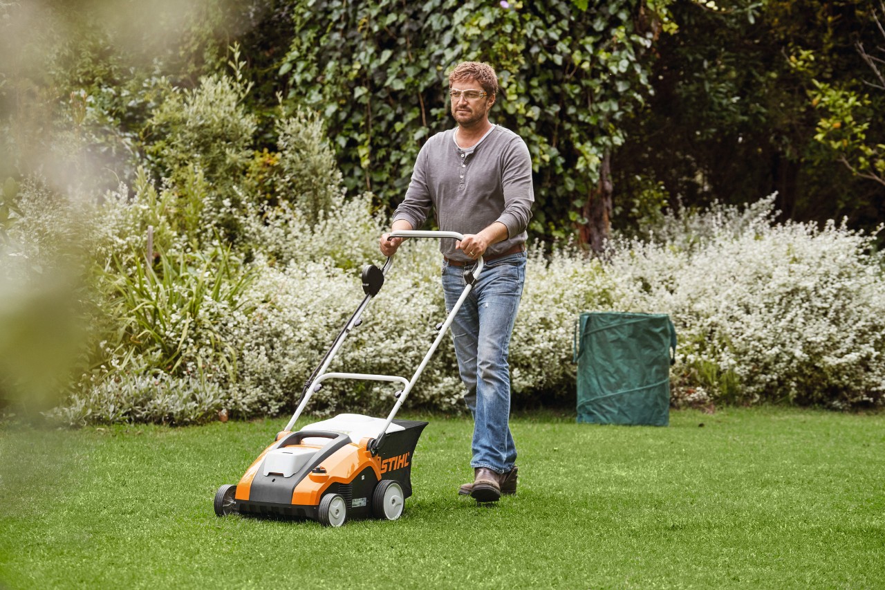Um homem escarifica o gramado verde com um arejador de grama a bateria STIHL RLA 240