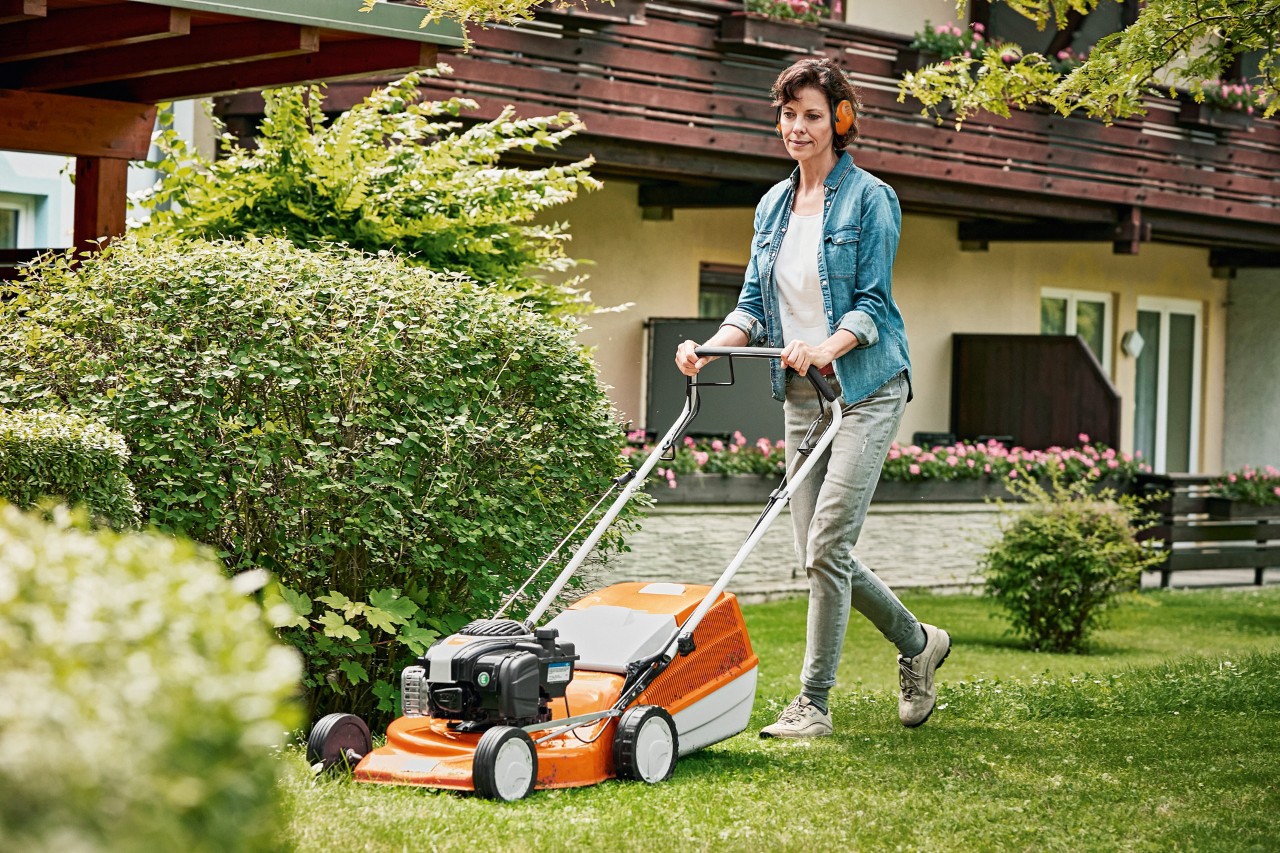 Uma mulher a utilizar um cortador de grama a gasolina STIHL RM 243 T no espaço verde, à frente de uma casa