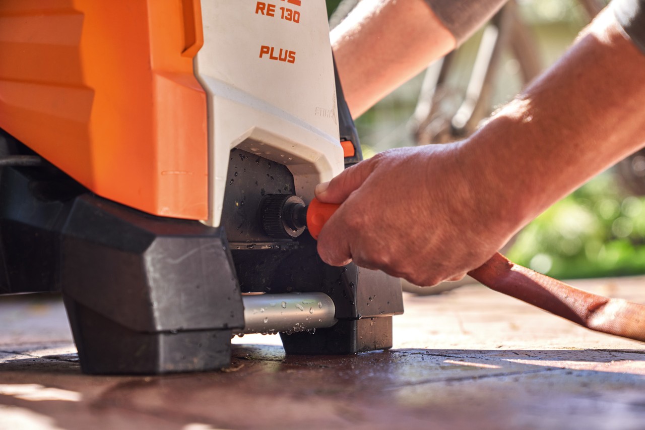Uma pessoa liga uma mangueira de jardim à lavadora de alta pressão STIHL RE 130 PLUS para a utilizar