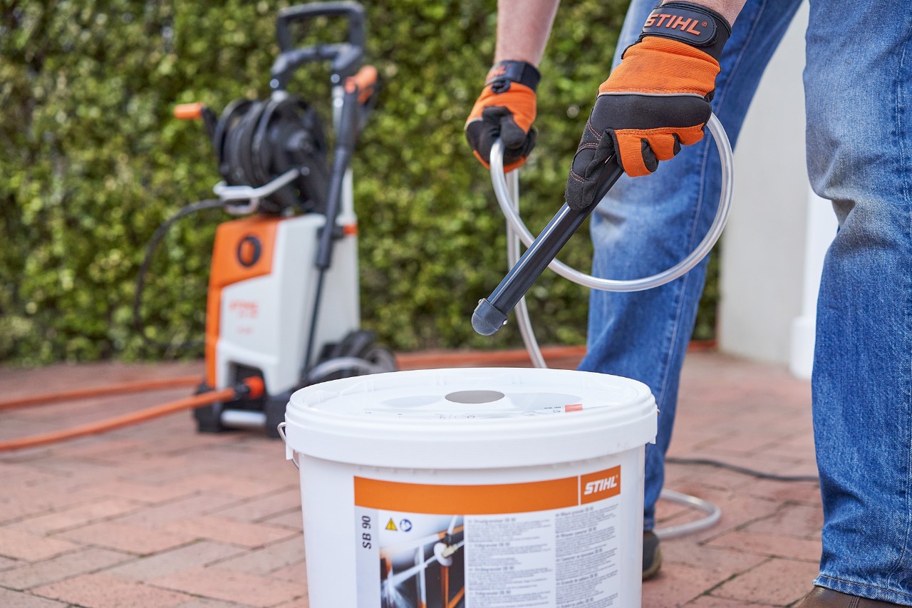 Um homem com luvas de trabalho à frente de uma lavadora de alta pressão usa a areia calibrada STIHL SB 90 para injeção de areia úmida 