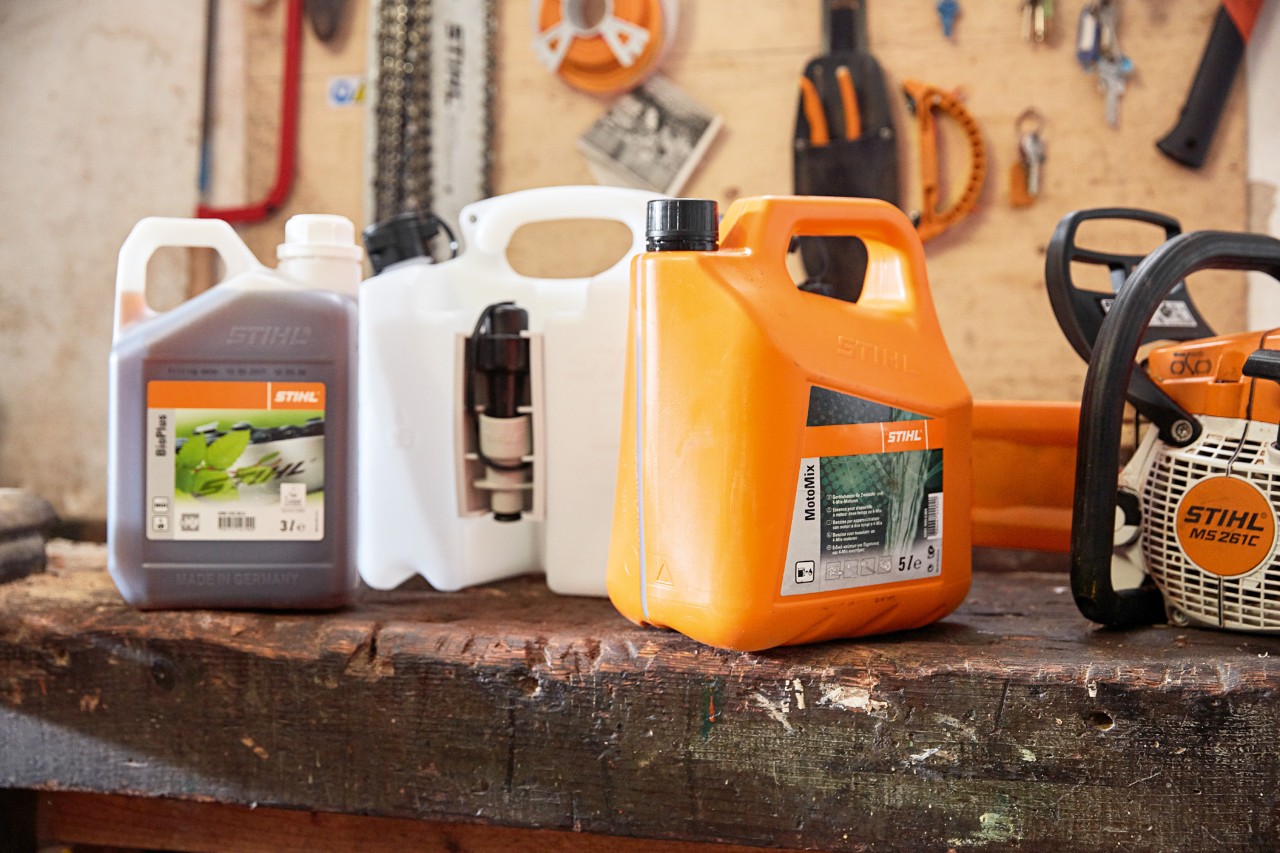 Jerricans com a mistura para motosserras STIHL MotoMix, óleo e gasolina, e uma motosserra a gasolina STIHL MS&nbsp;261&nbsp;C numa oficina