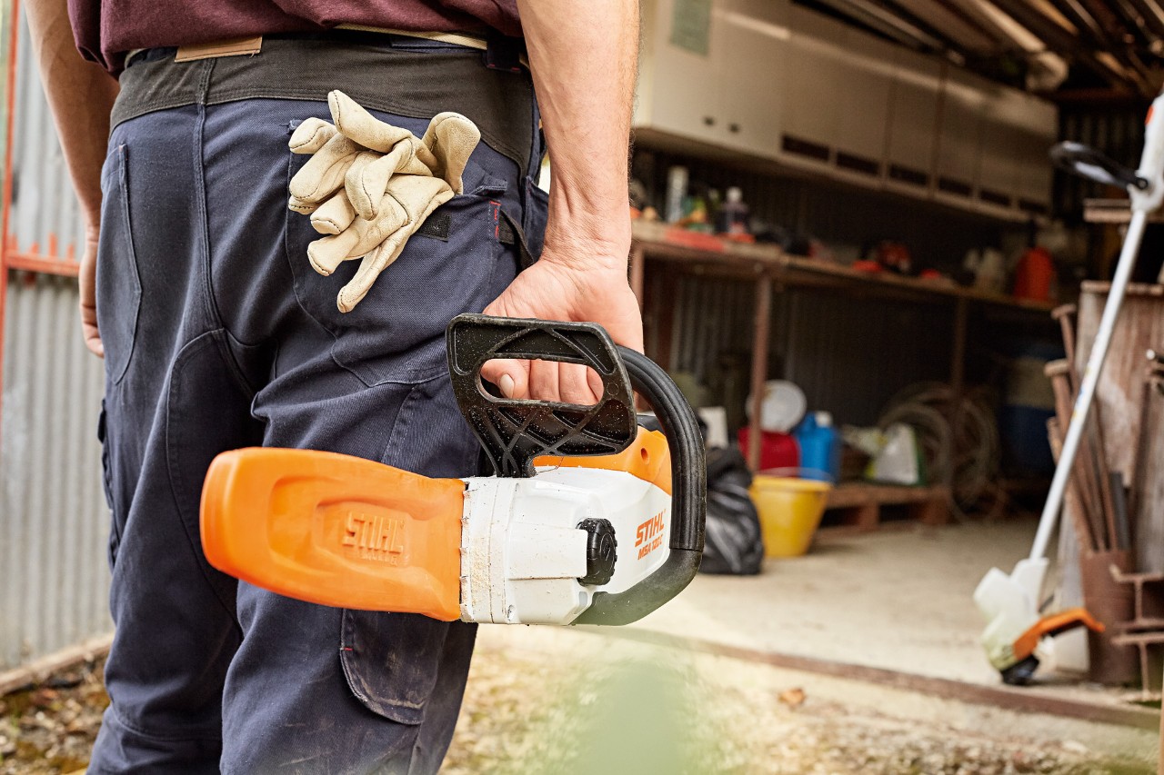 Um homem a encaminhar-se para uma oficina levando uma motosserra a bateria STIHL com protetor de corrente