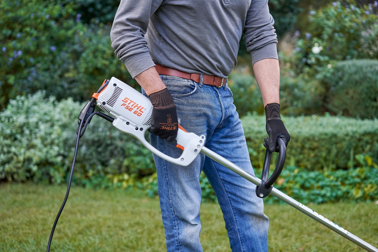 Um homem com luvas de proteção segura na motorroçadora elétrica STIHL FSE&nbsp;60 com as duas mãos