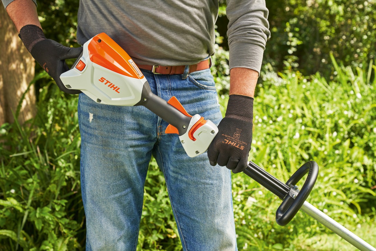Um homem de luvas de proteção verifica a bateria da motorroçadora a bateria STIHL FSA&nbsp;60 para a ligar