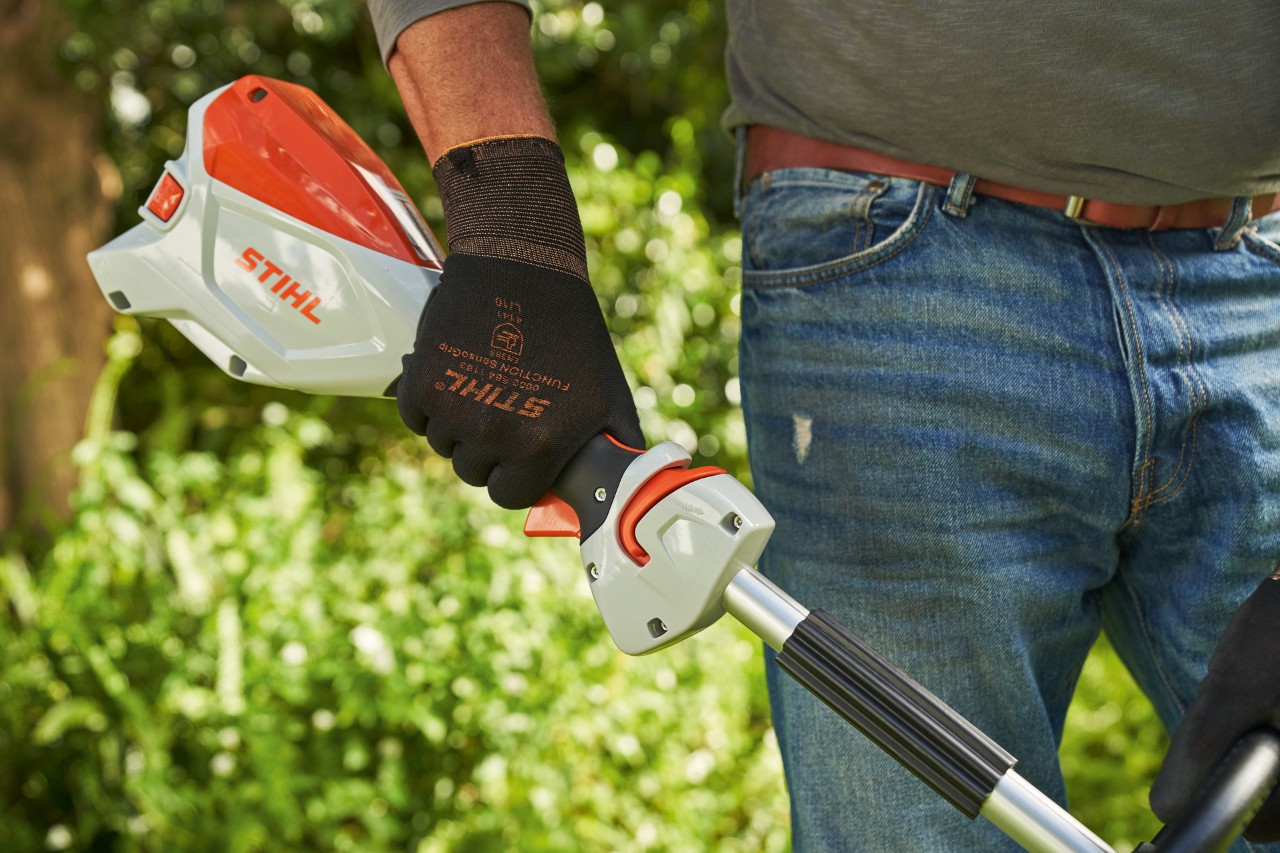 Um homem de luvas de proteção prime a corrediça de desbloqueio da motorroçadora a bateria STIHL FSA&nbsp;60 