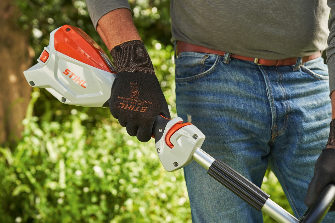 Um homem de luvas de proteção aciona a alavanca de comando da motorroçadora a bateria STIHL FSA&nbsp;60 para a ligar