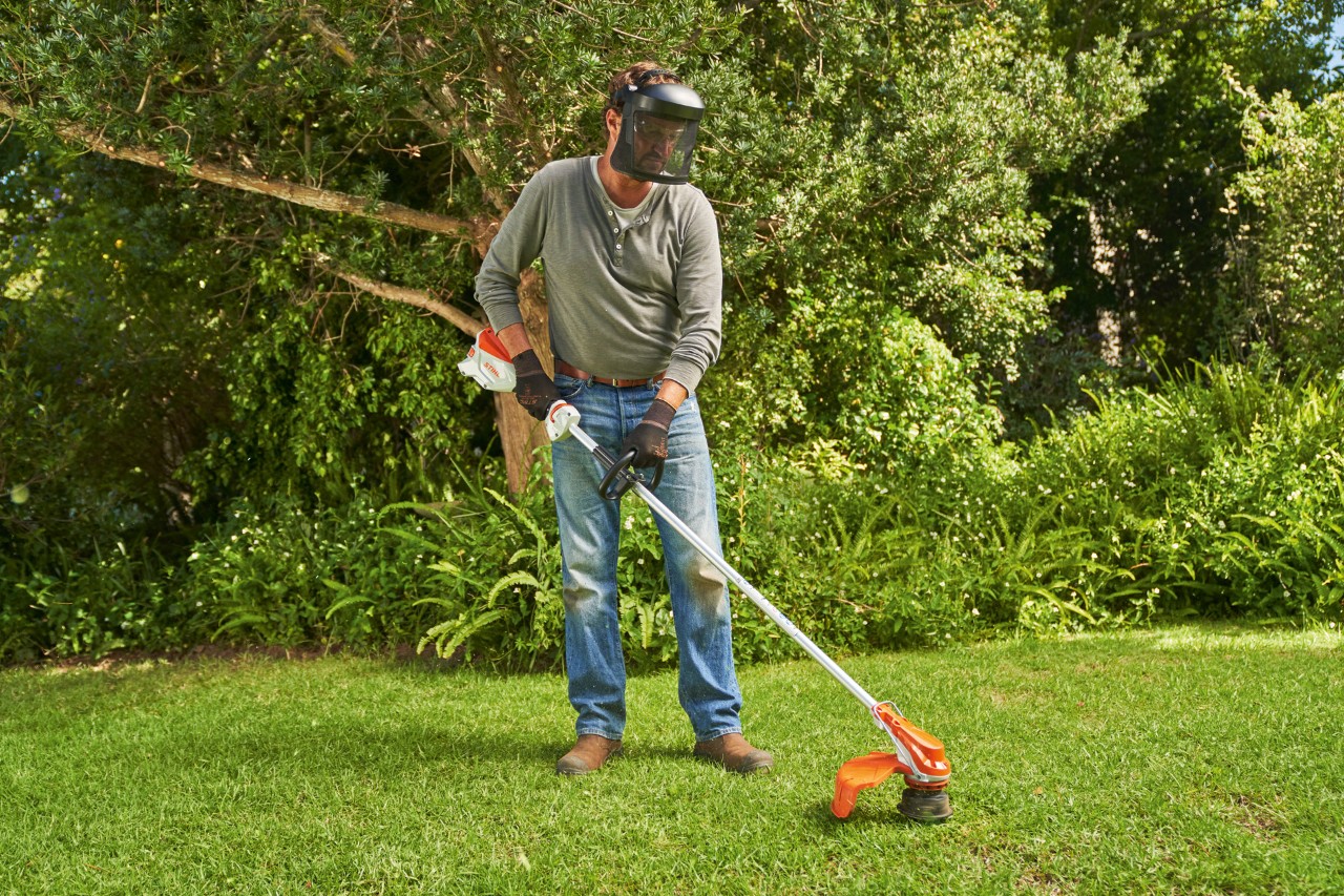Um homem de viseira corta a relva num jardim com a motorroçadora a bateria STIHL FSA&nbsp;60