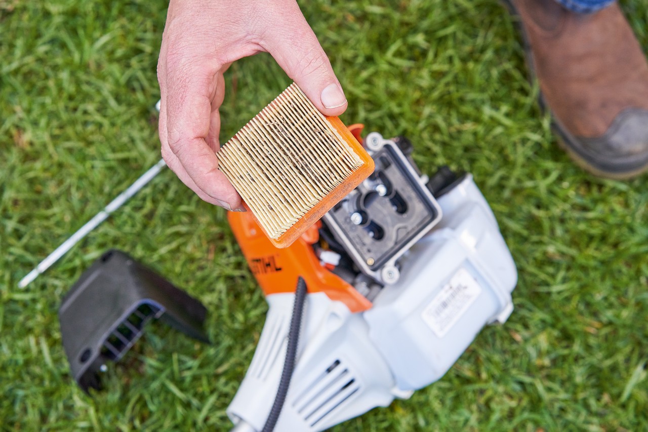 Alguém retira o filtro de ar de uma roçadeira STIHL para limpa-lo 