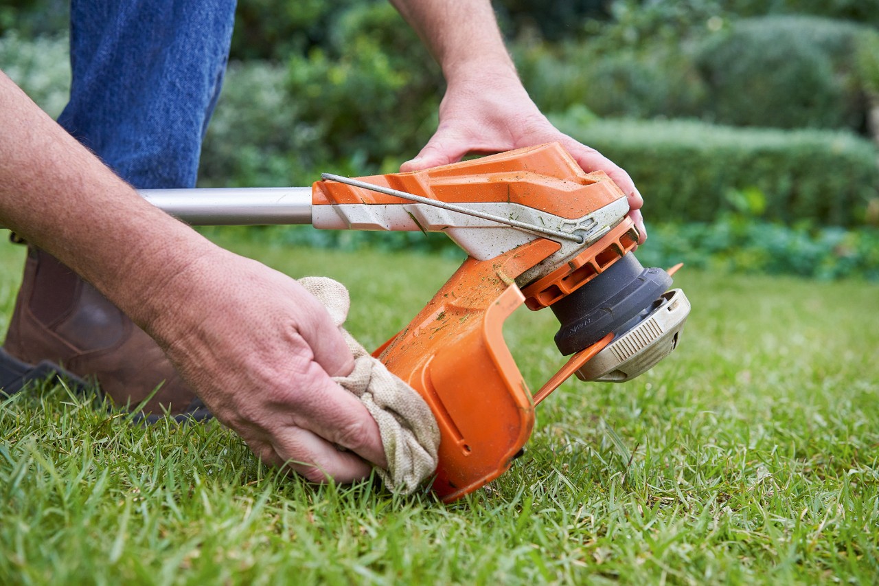 Alguém limpa com um pano úmido a proteção de uma roçadeira STIHL