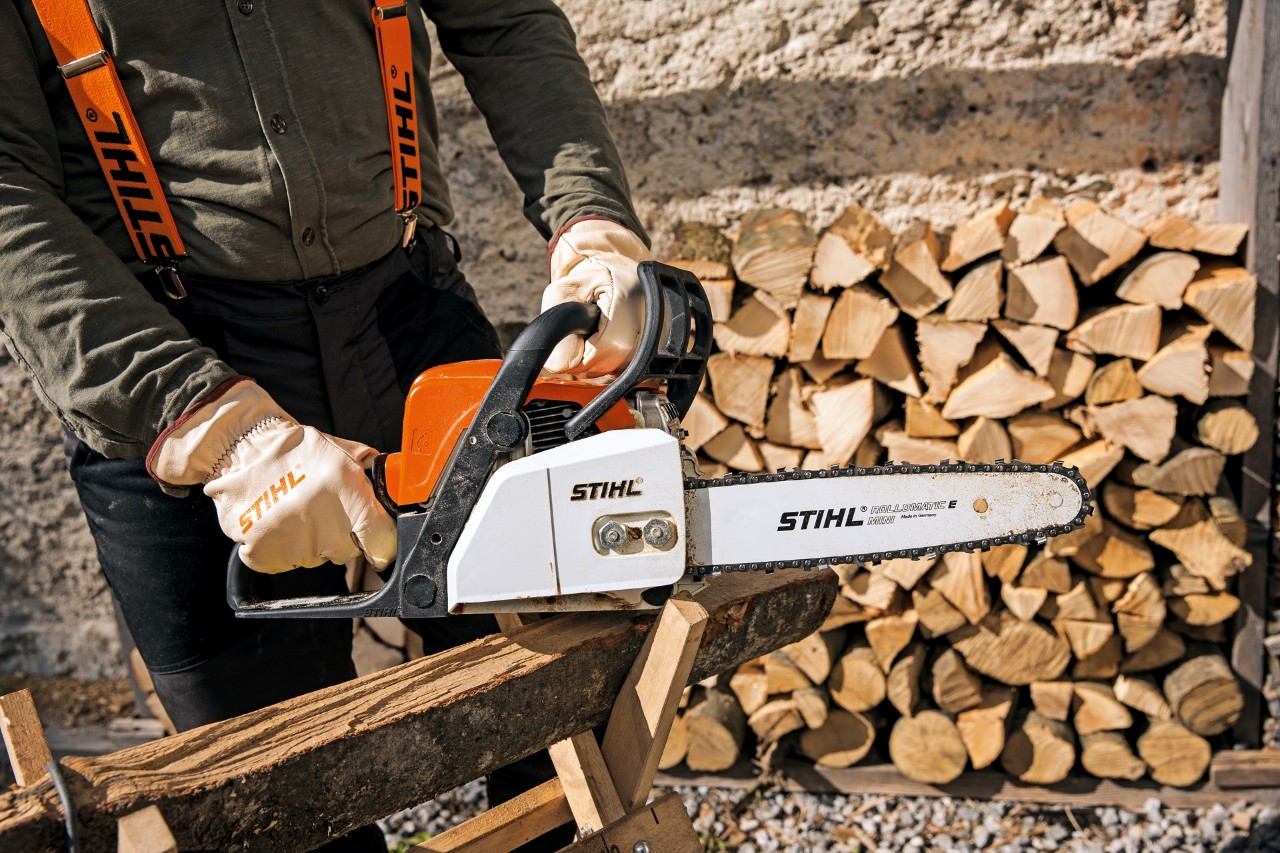 Alguém com vestuário de proteção pousa uma motosserra a gasolina STIHL MS 170 sobre uma extensão de madeira num cavalete