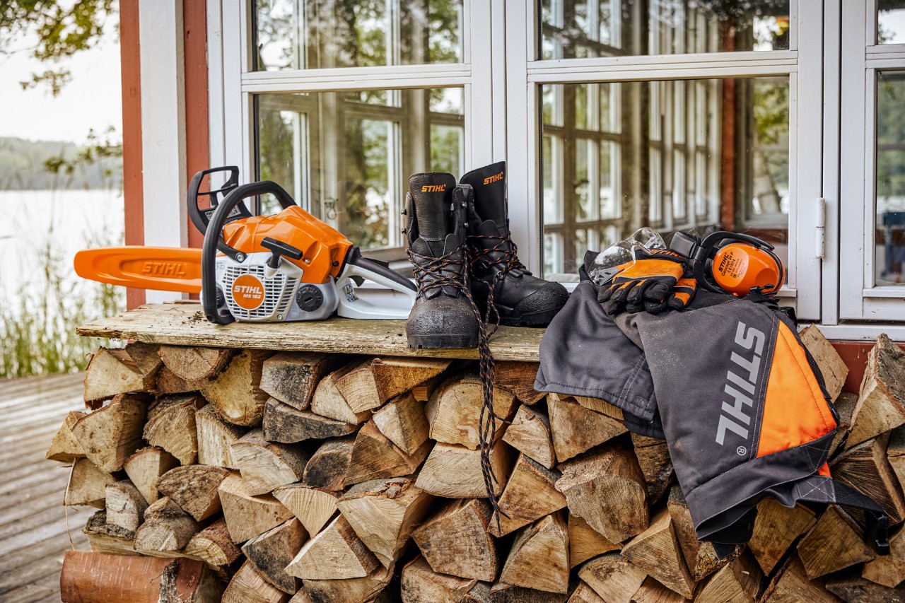 Vestuário de proteção STIHL e uma MS&nbsp;162 num lenheiro, sobre lenha empilhada