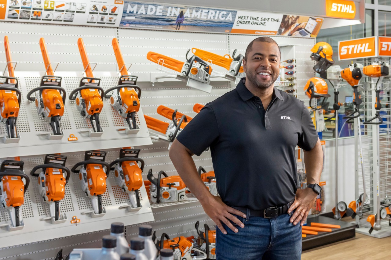 Homem sorrindo parado na frente de mostruario de máquinas STIHL