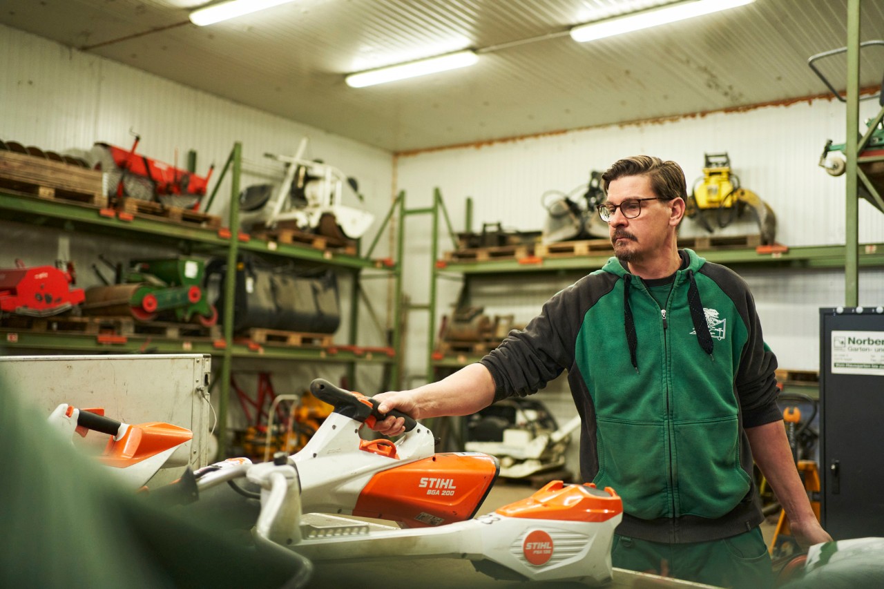 Um homem numa oficina atrás de uma superfície de trabalho com máquinas a bateria STIHL agarra no soprador a bateria STIHL BGA 200