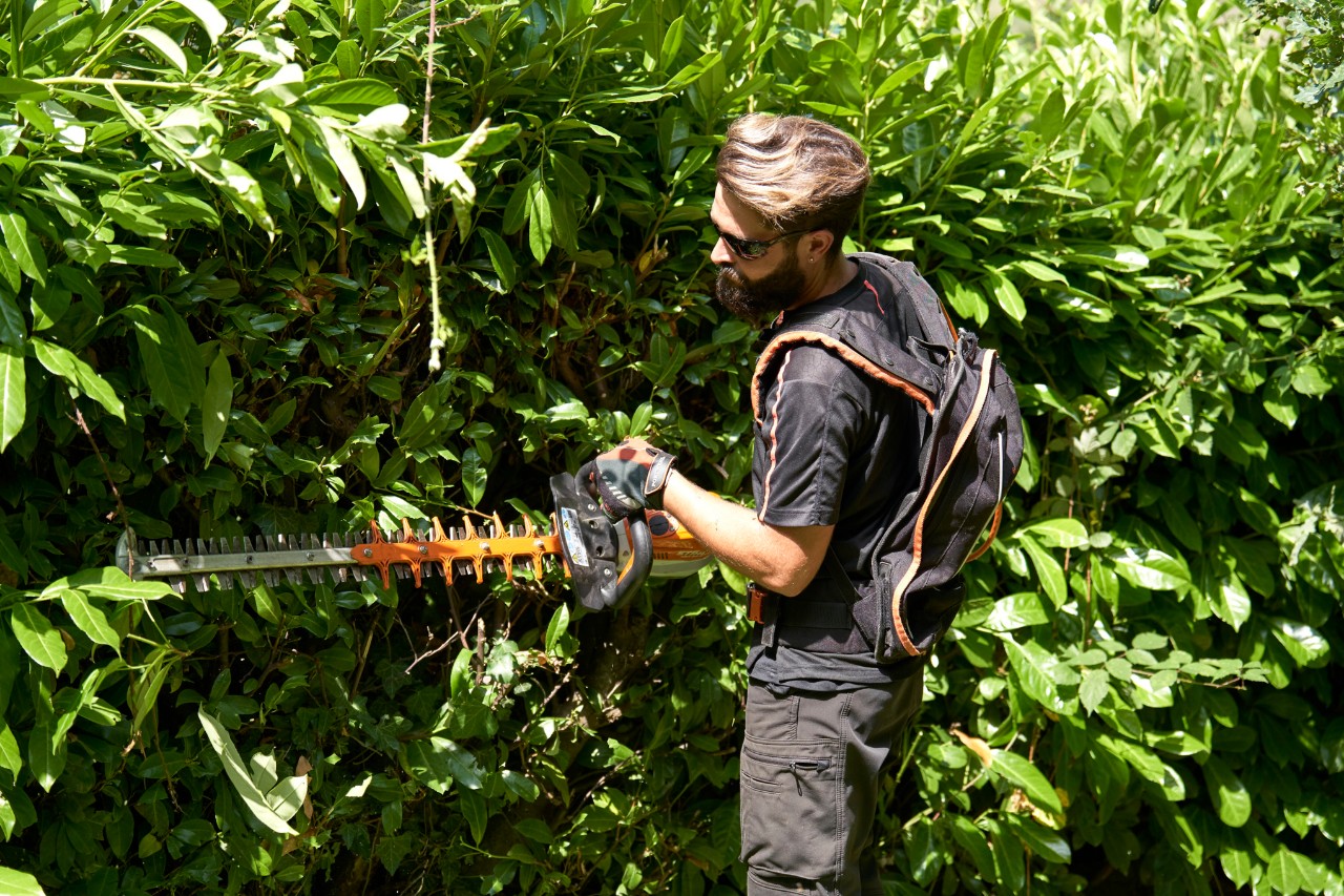 Um profissional com equipamento de proteção a cortar um arbusto com uma podadora a bateria STIHL