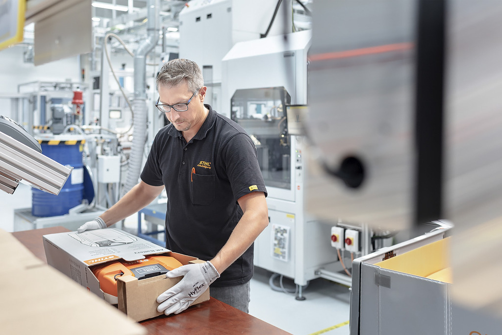 Um funcionário na produção de baterias a embalar uma máquina a bateria STIHL numa caixa de cartão 