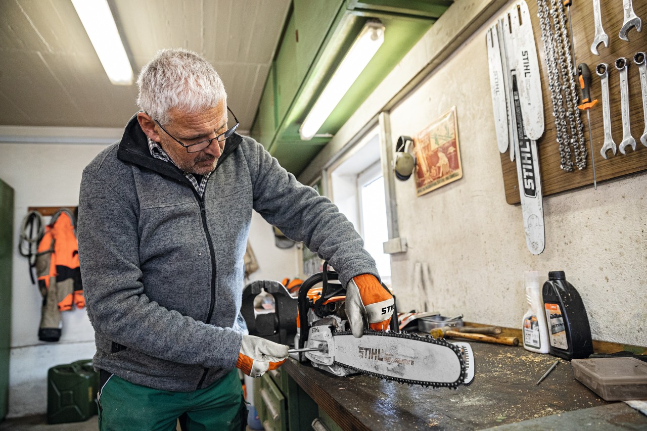 Um homem numa oficina a trabalhar numa motosserra com sabre STIHL Rollomatic E 