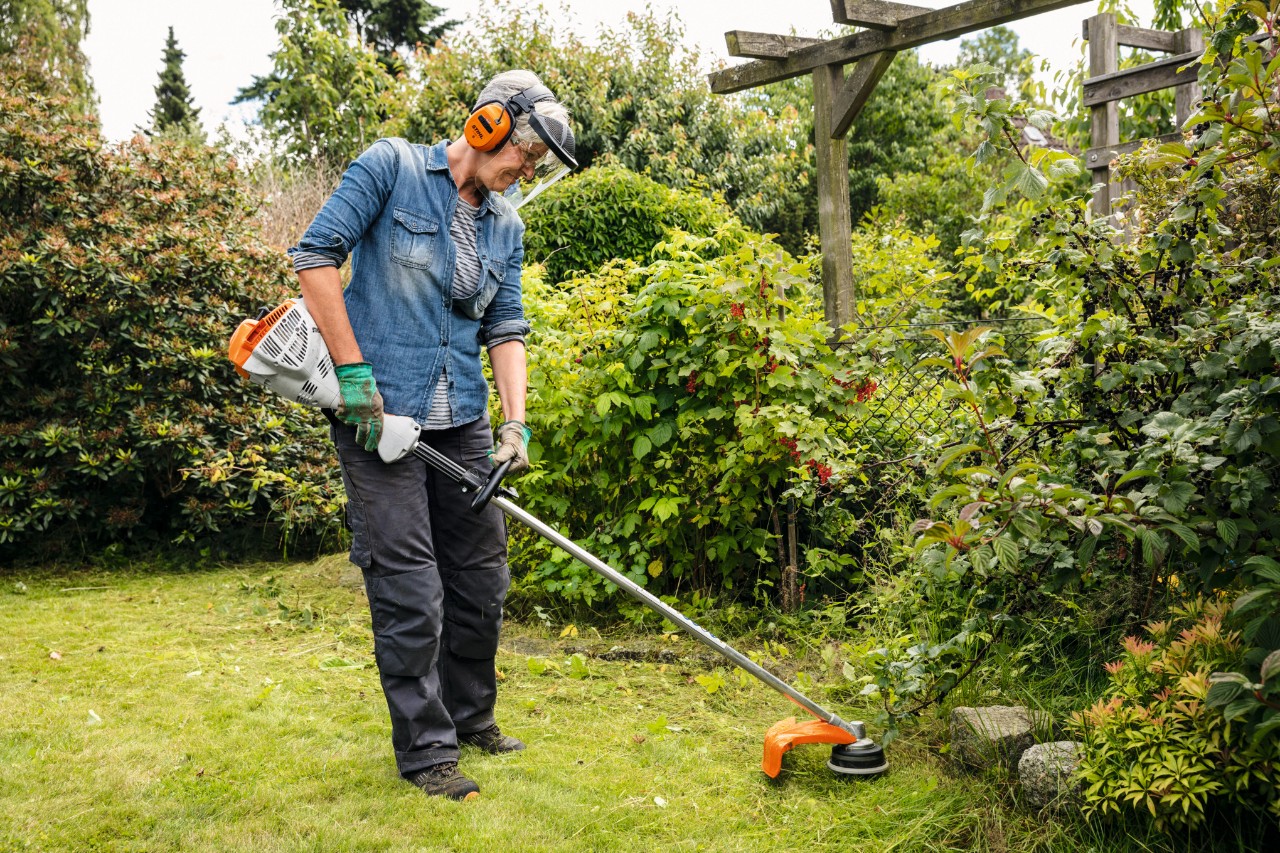 Um trabalhador florestal com vestuário de proteção STIHL, incluindo calças Dynamic Vent (categoria de proteção anticorte 1) a serrar uma árvore na floresta com uma motosserra STIHL