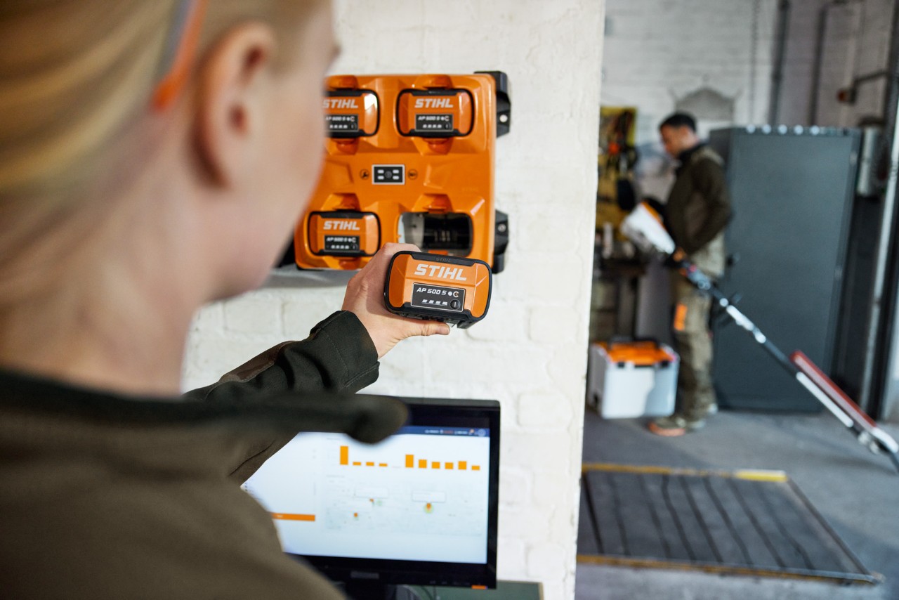Uma mulher frente a um portátil a retirar uma AP 300 S do multicarregador STIHL AL 301-4