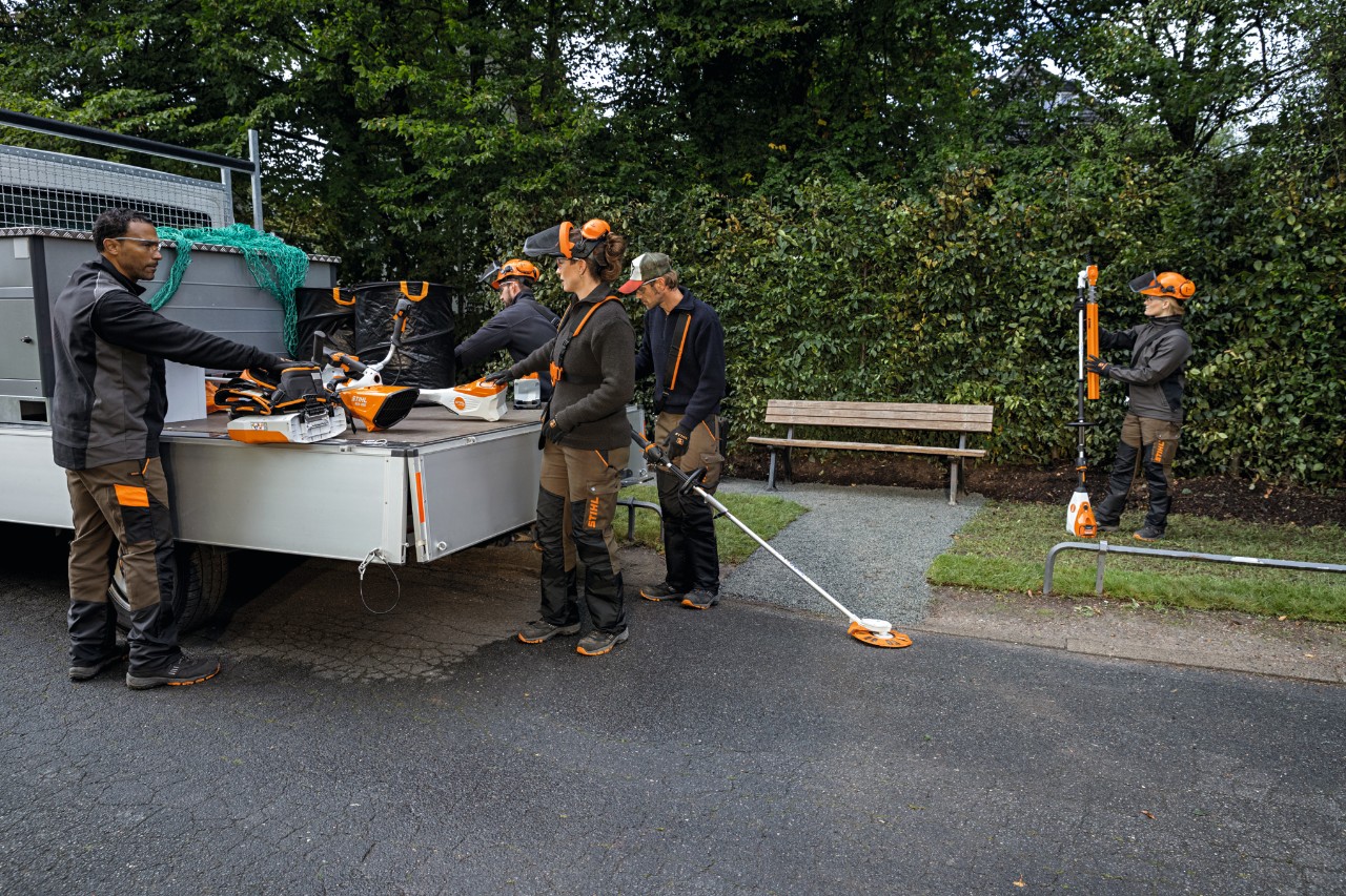 Jardineiros e paisagistas a descarregar máquinas do sistema AP da STIHL e uma bateria de mochila da superfície de carga do seu veículo. 