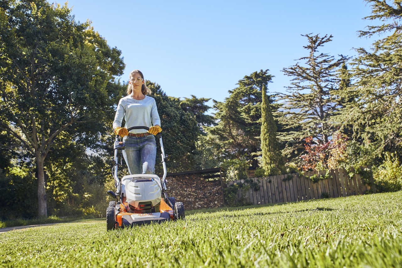 Uma mulher com um cortador de grama a bateria da STIH em seu jardim