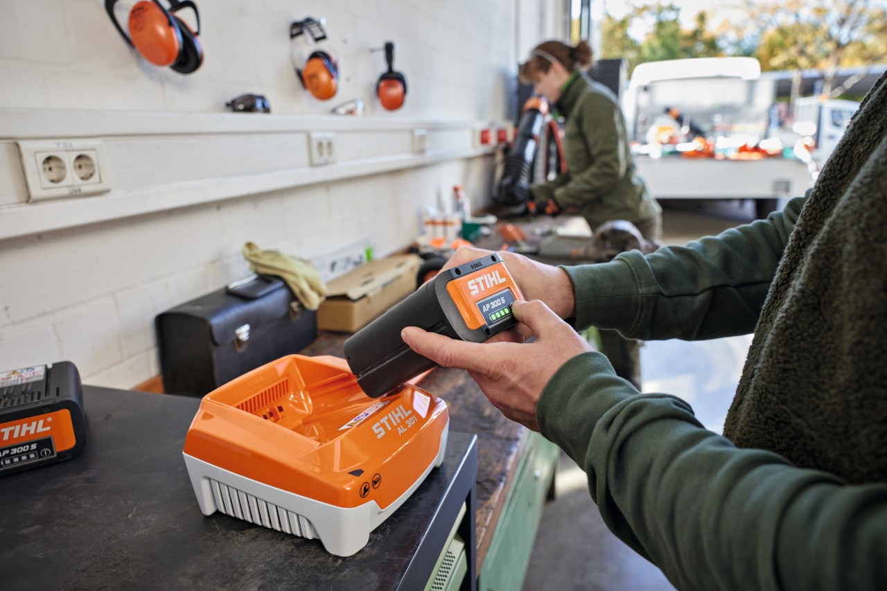 Uma pessoa insere uma bateria STIHL AP 300 S num carregador rápido STIHL AL 301