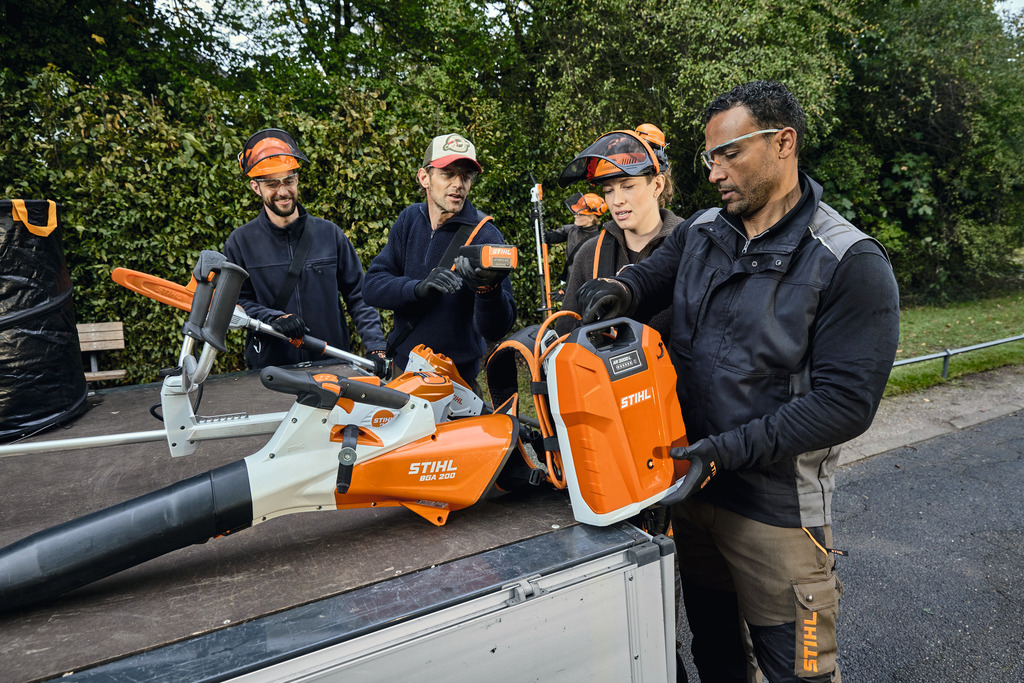 Uma equipa de profissionais de paisagismo descarrega o seu equipamento profissional STIHL a bateria da área de carga de um veículo.
